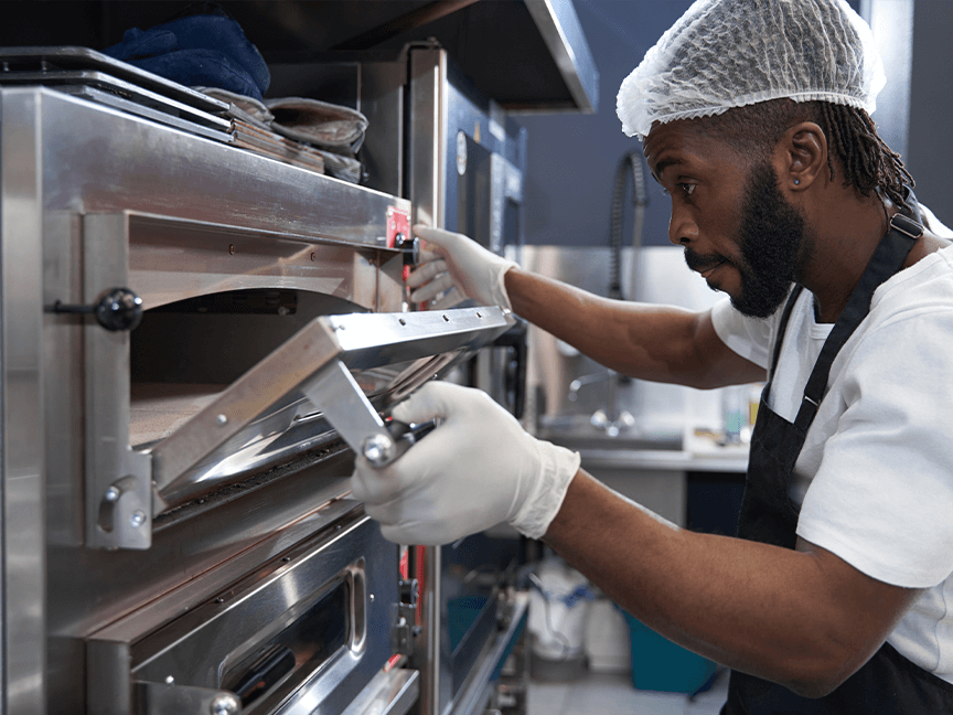 Man with hairnet checking a pizza oven